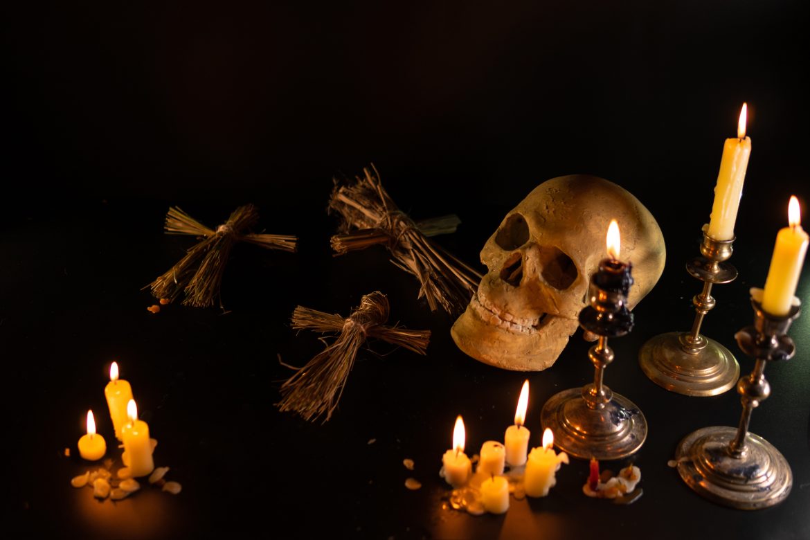 Old Skull and candle with incense on old altar plate which has dim light. Select focus, black background. Straw voodoo dolls. Copy space