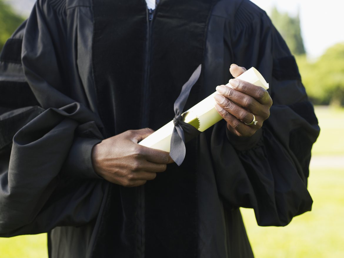 Mature woman in graduation gown holding diploma, mid section Lucky charms and spells