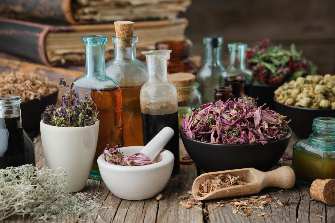 Bottles of healthy tincture or infusion, mortar and bowls of medicinal herbs, old books on table. Herbal medicine. Traditional Herbs